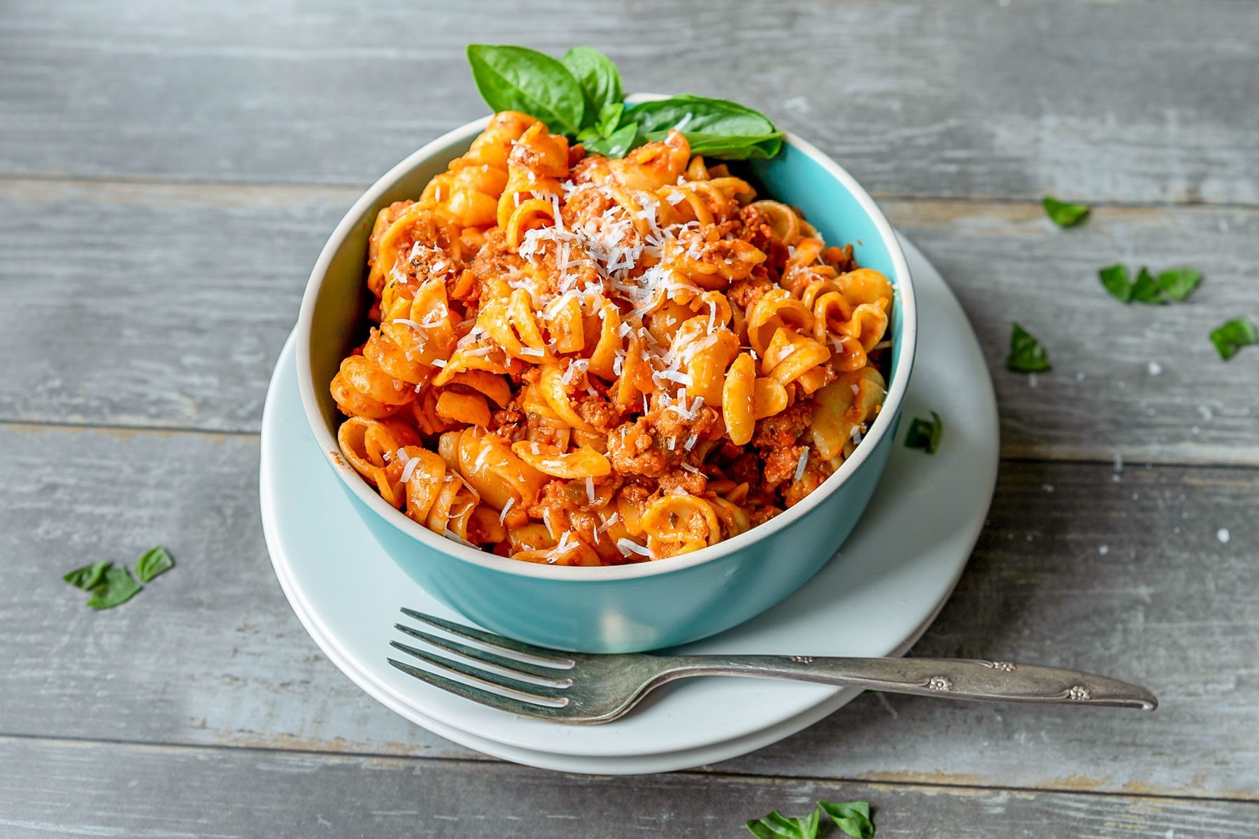 Emily Blunt’s Turkey Bolognese served in a small bowl with fork and plates on wooden surface