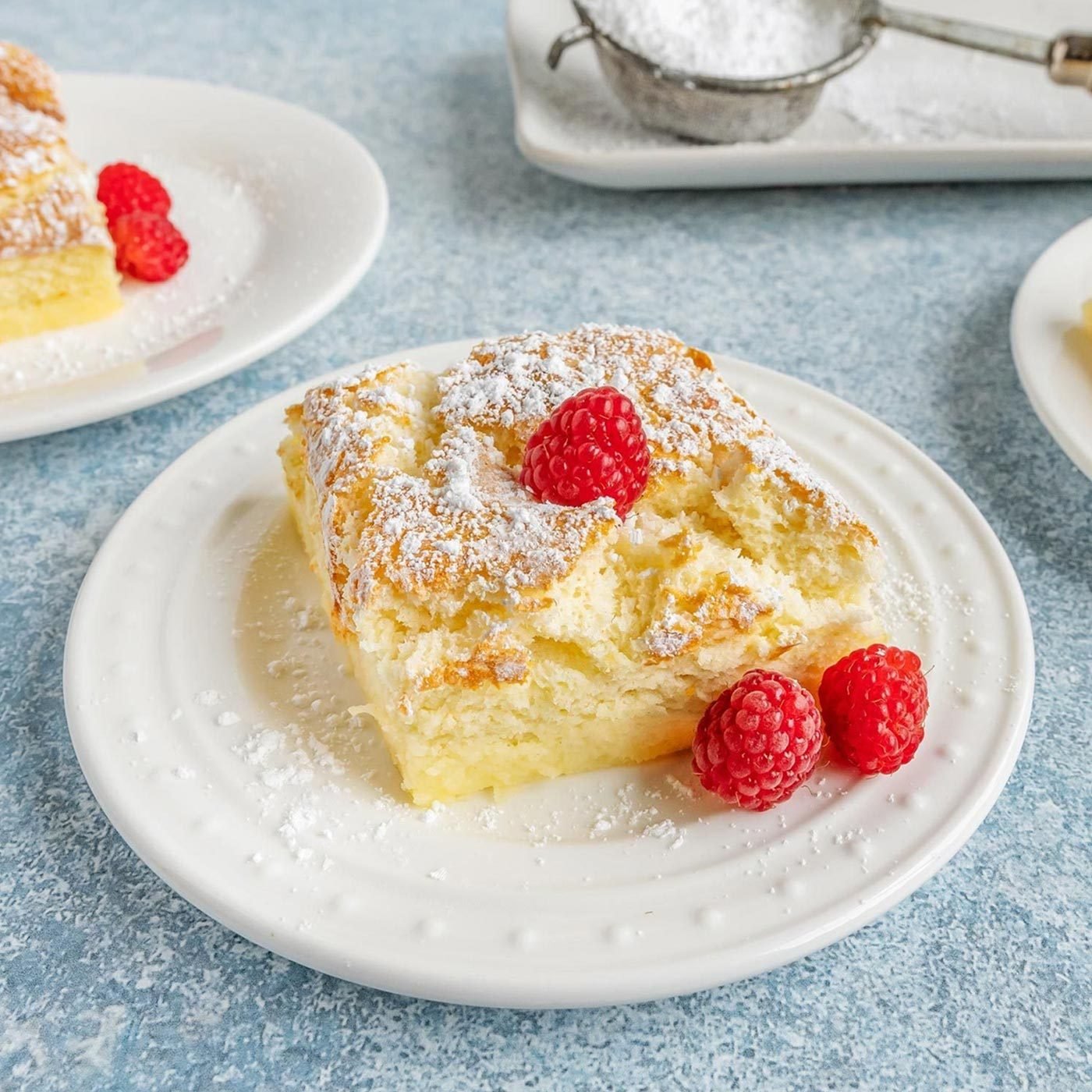 Square slice of Magic Cake on a plate topped with raspberries