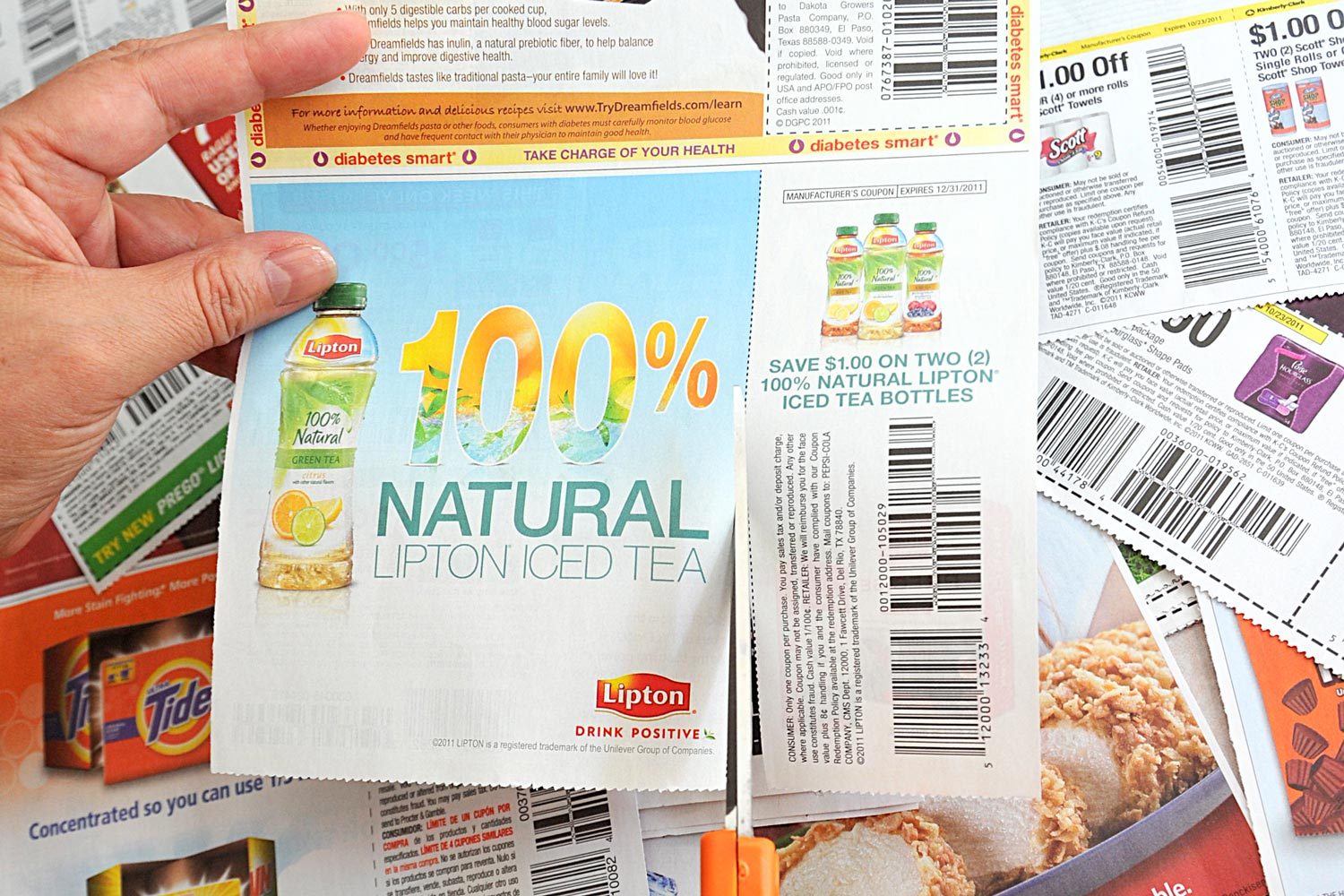 Woman Cuts Coupons from advertisement section of the Sunday Newspaper with bright orange scissors