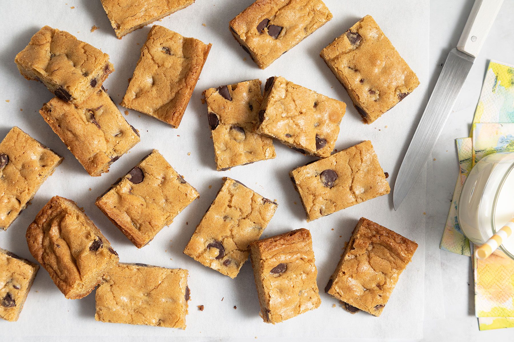 Chocolate Chip Blondies on white surface with glass of milk