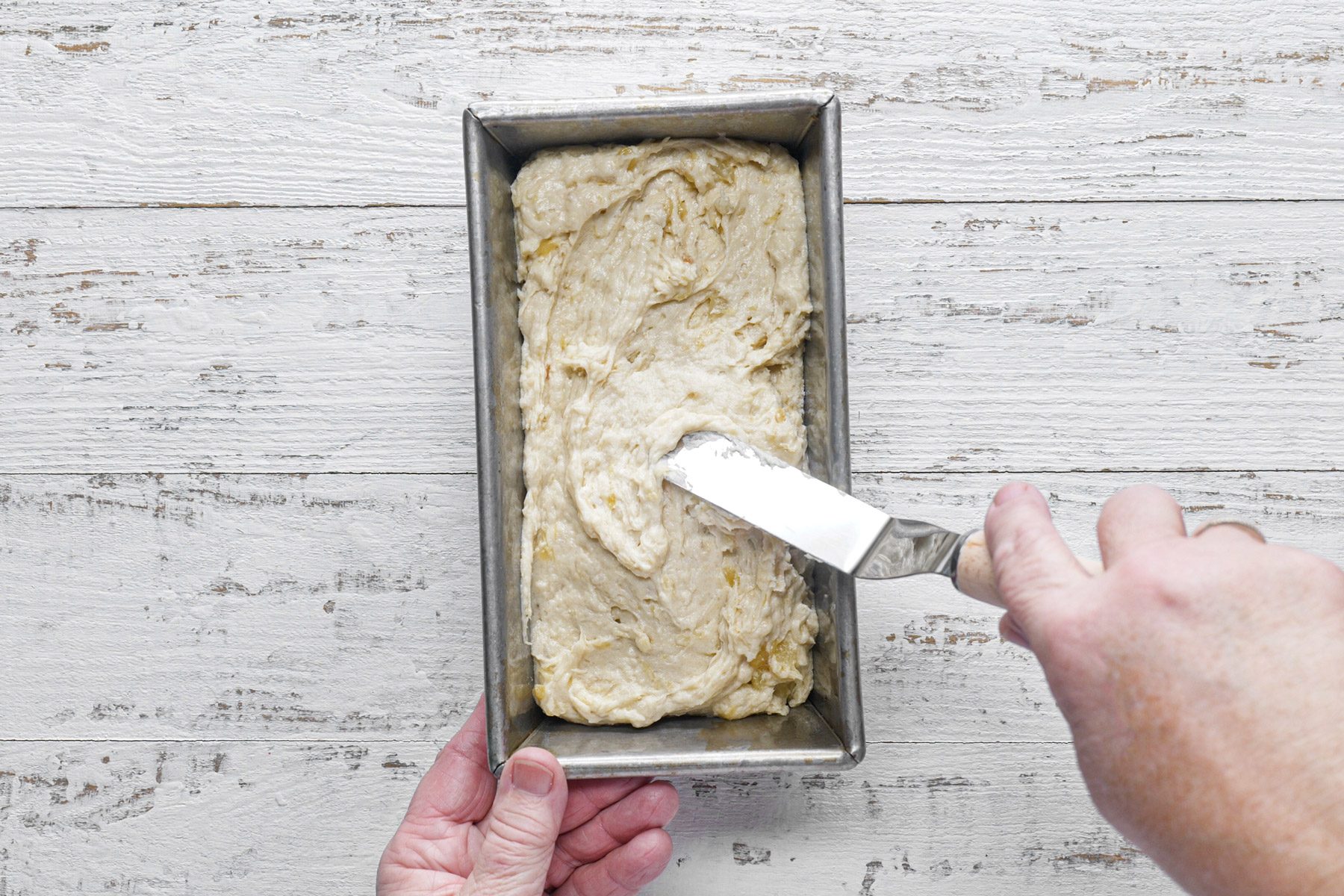 A person holding a spatula over a loaf of banana bread