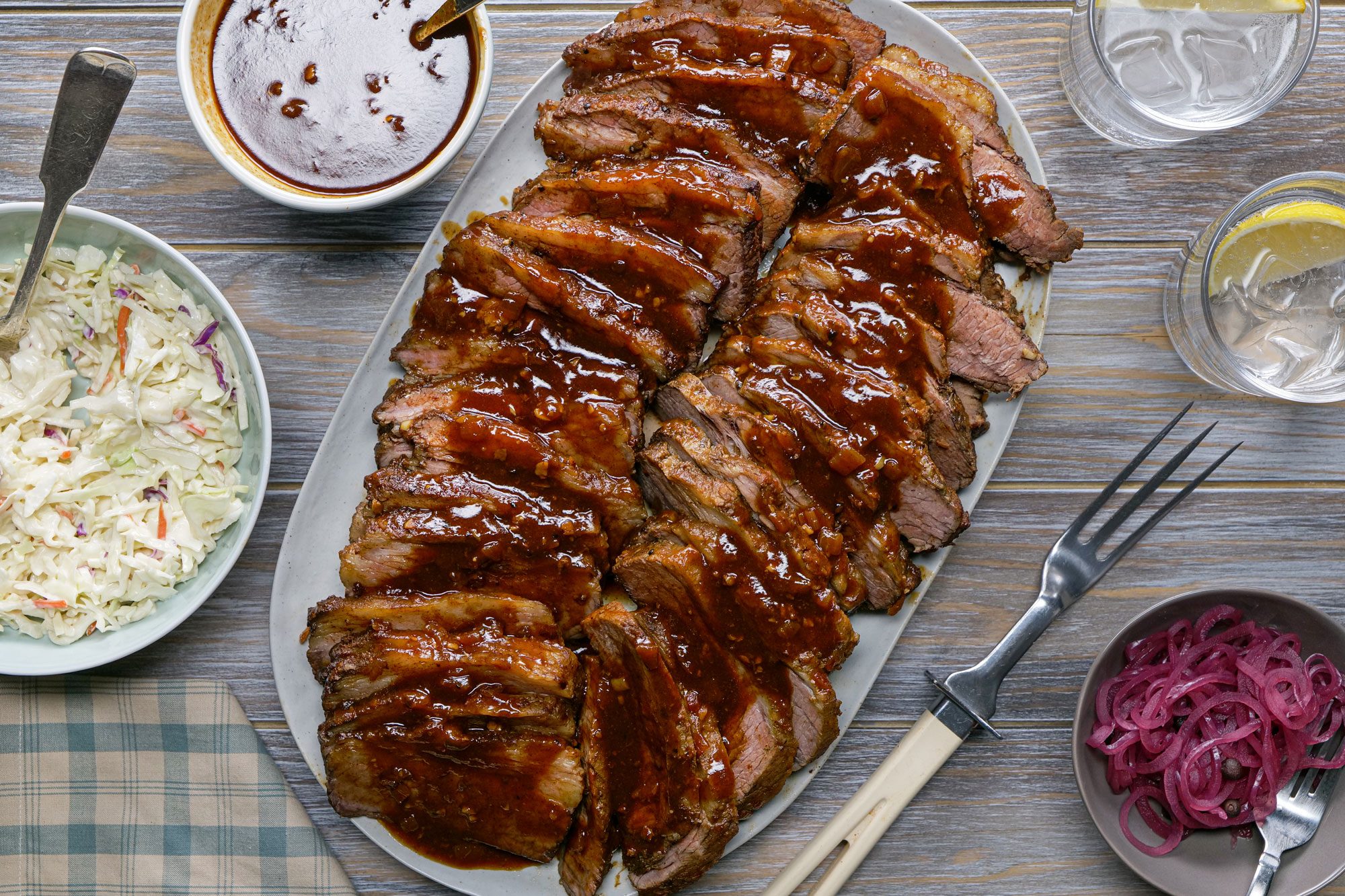 Delicious Slow Cooker Brisket served in a plate with barbecue sauce, salad and beverages