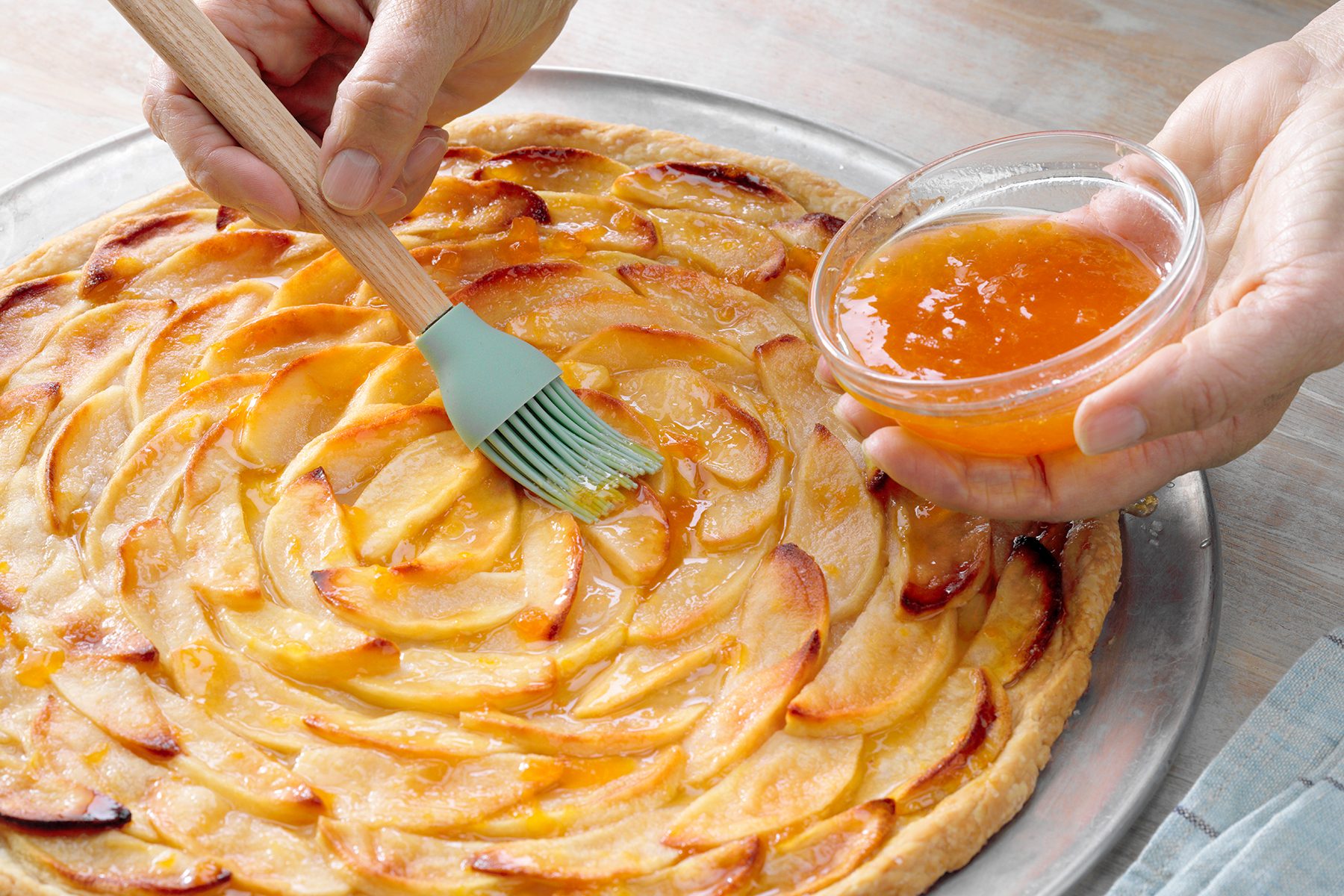 A person is brushing apple pie with butter
