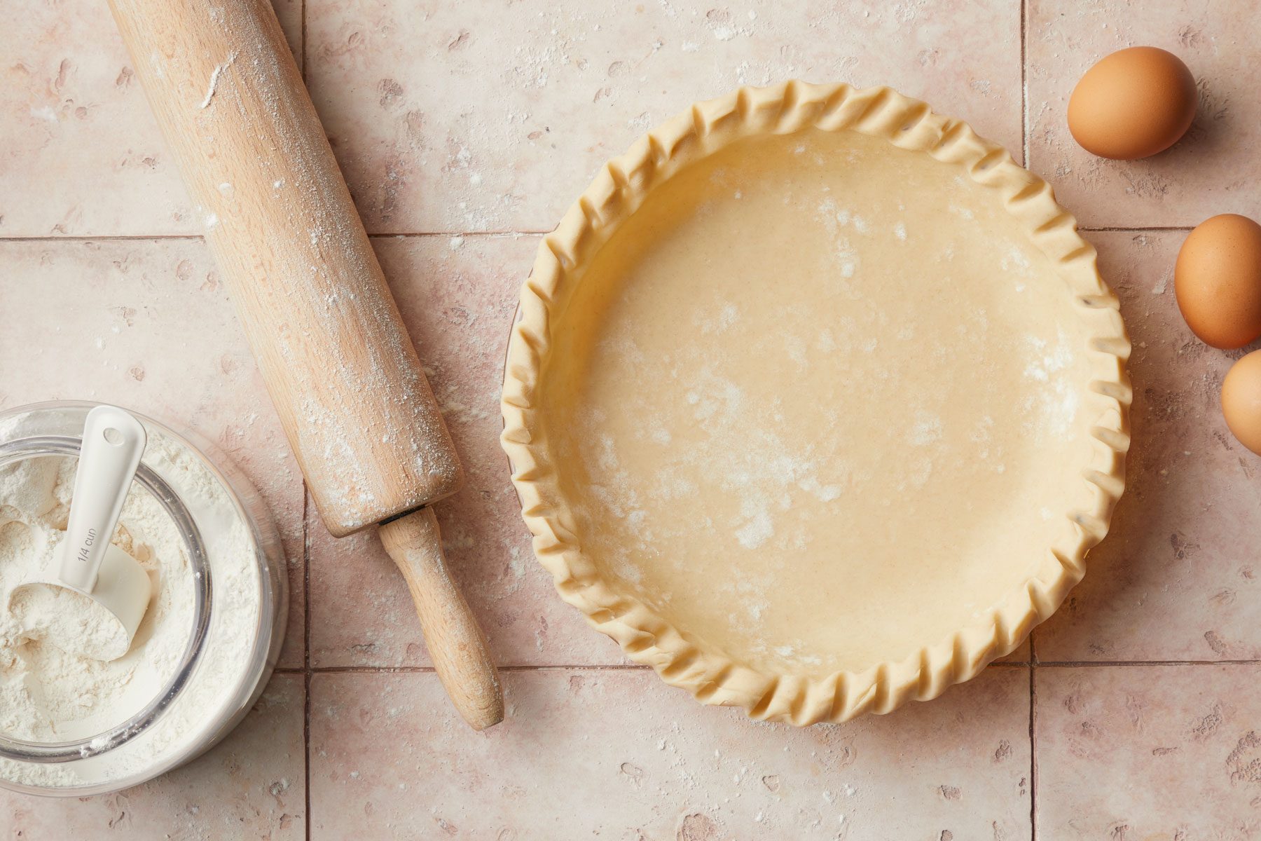 Pie crust roller pin eggs and flour on a kitchen countertop