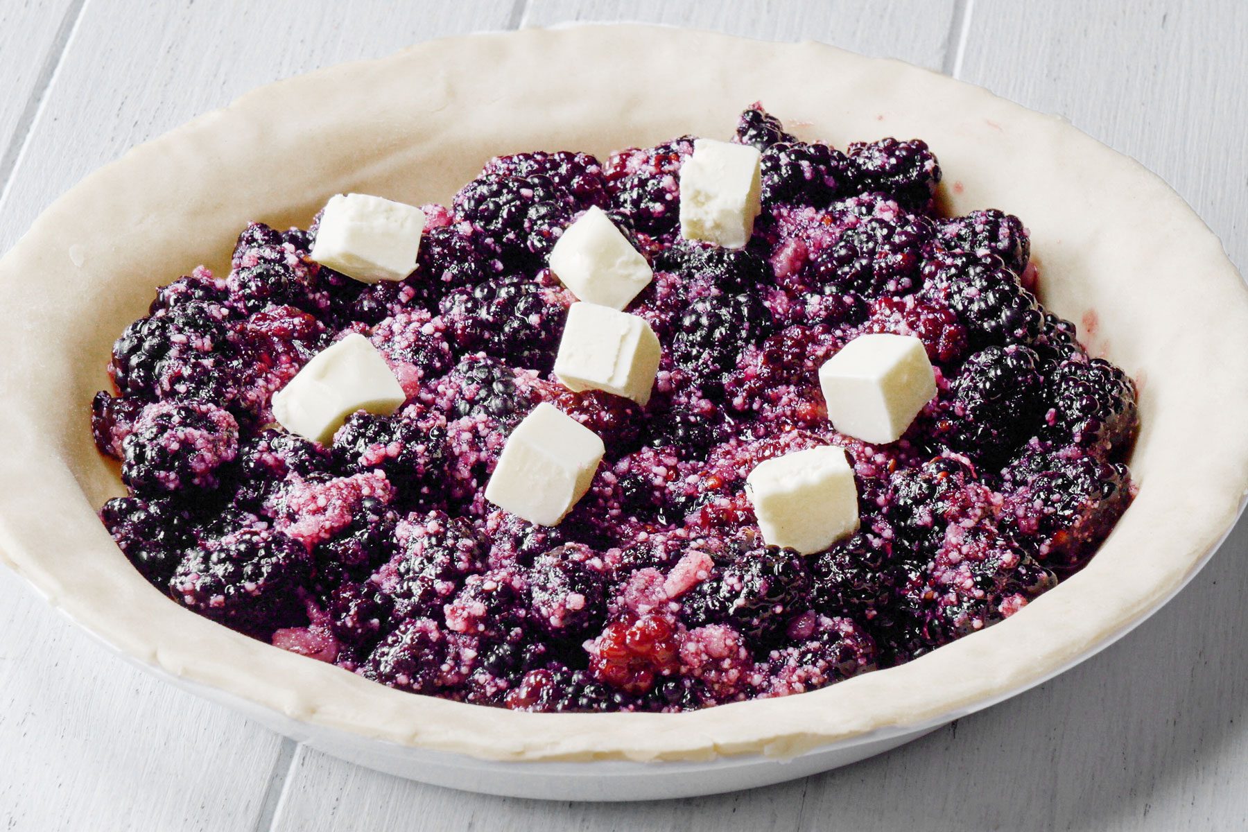 Butter pieces and black berry mixture on pie crust