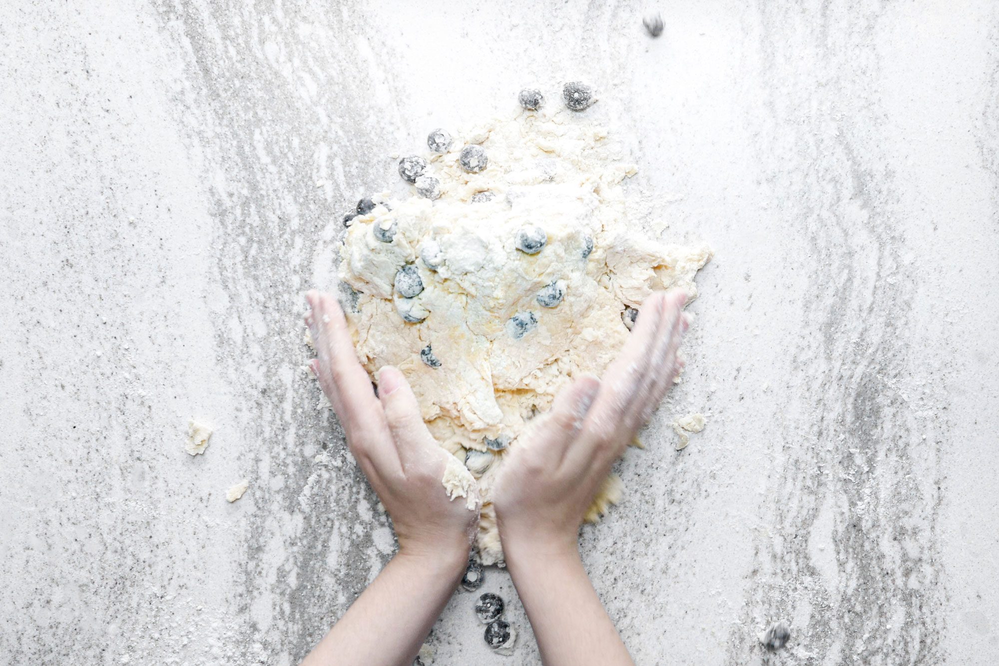 a person kneading Blueberries into dough on marble surface