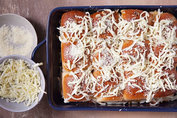 Sprinkled cheese on sliders on a baking tray