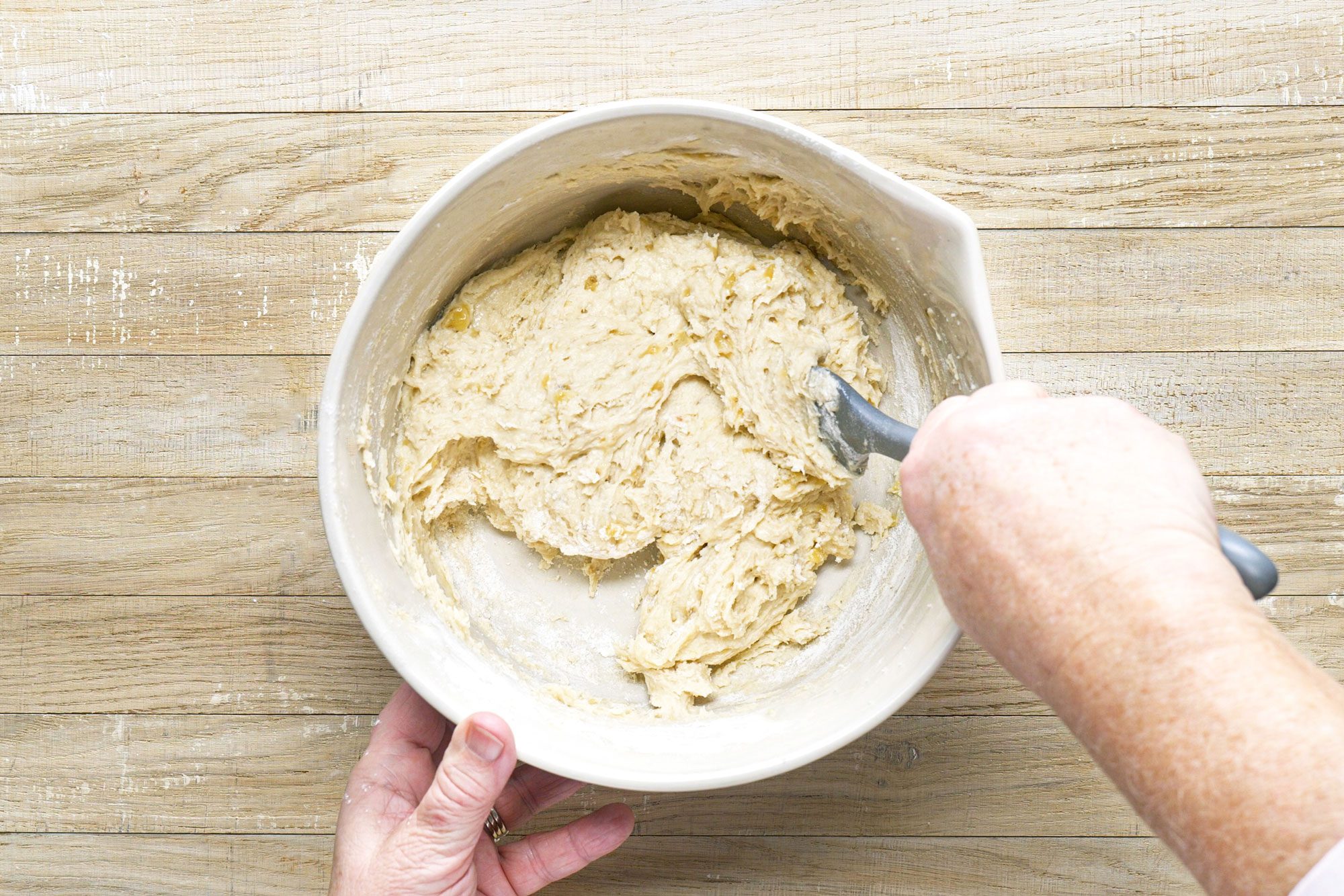a person folding Chocolate Chip Banana Bread Batter in a large bowl on a wooden surface