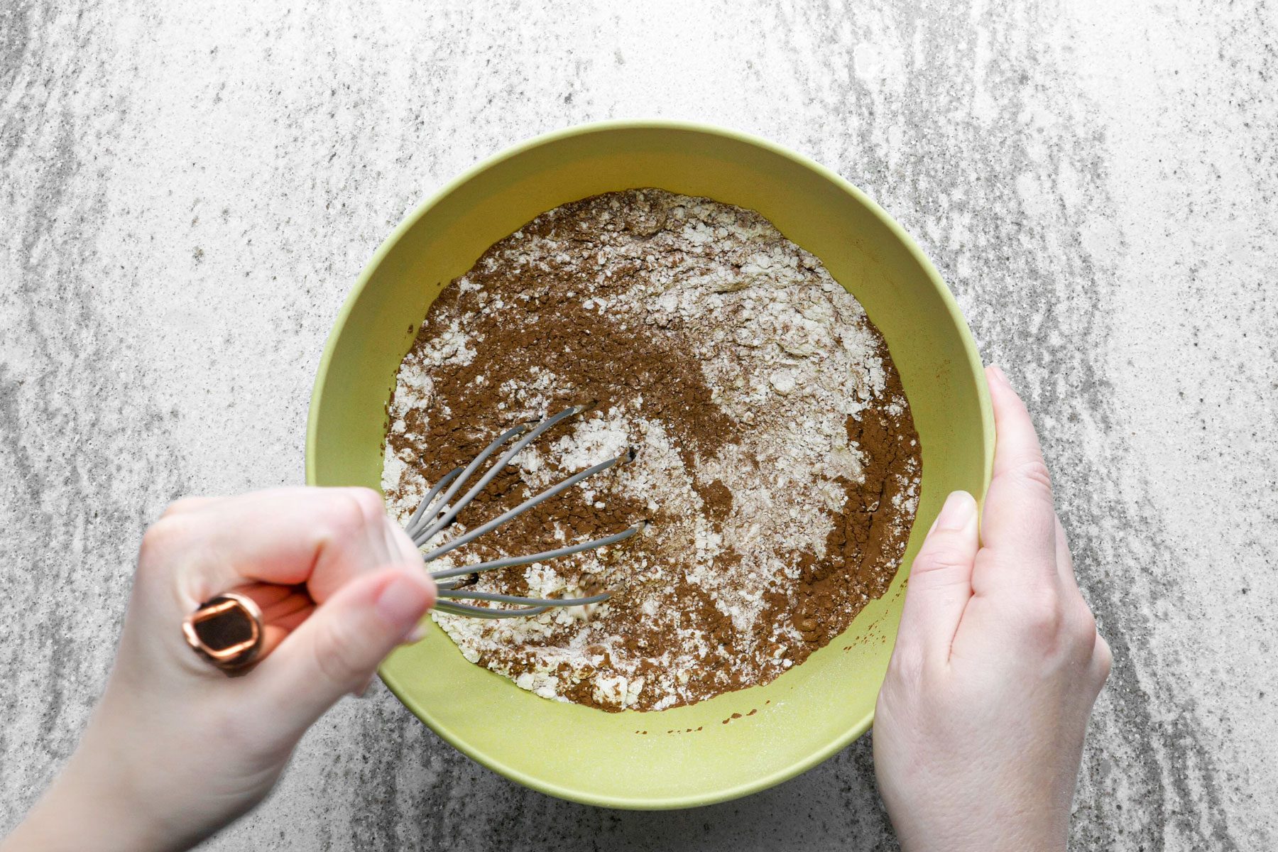 A person whisking flour, baking cocoa in a large bowl.