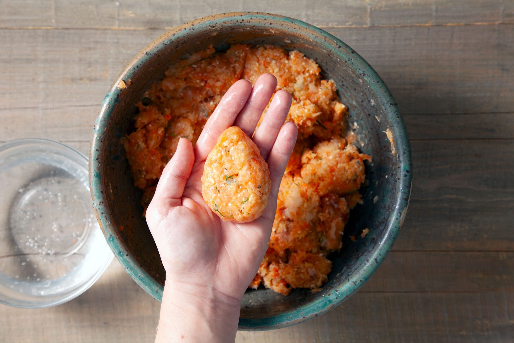 Holding fish mixture with a large bowl of fish mixture on a wooden table