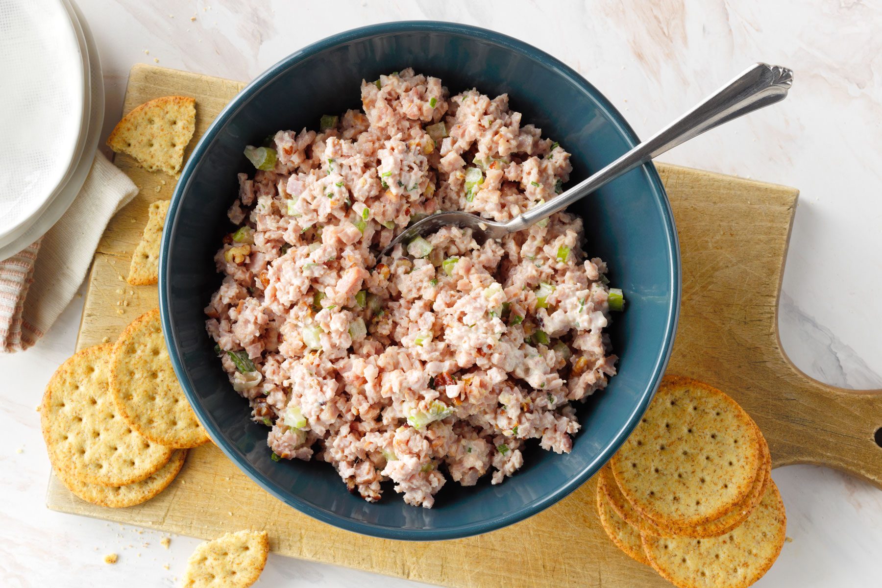 Ham Salad is served in a large bowl with crackers, placed on a wooden tray.