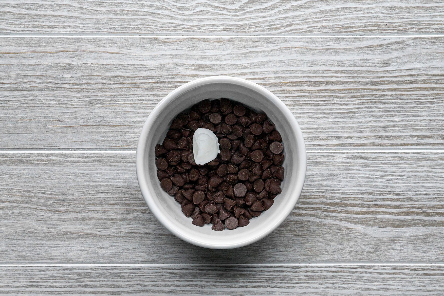 Bowl of chocolate chips with piece of coconut butter in it