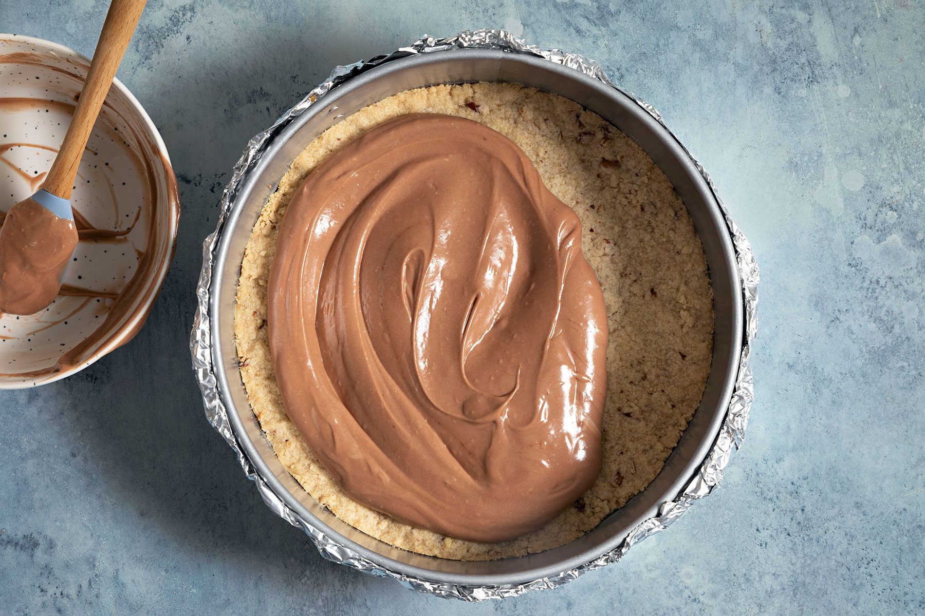Adding the chocolate mixture over baked crust in baking tray