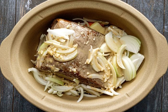 Onions, Rump Roast, Carrots and Potatoes in a Slow Cooker on a Wooden Surface