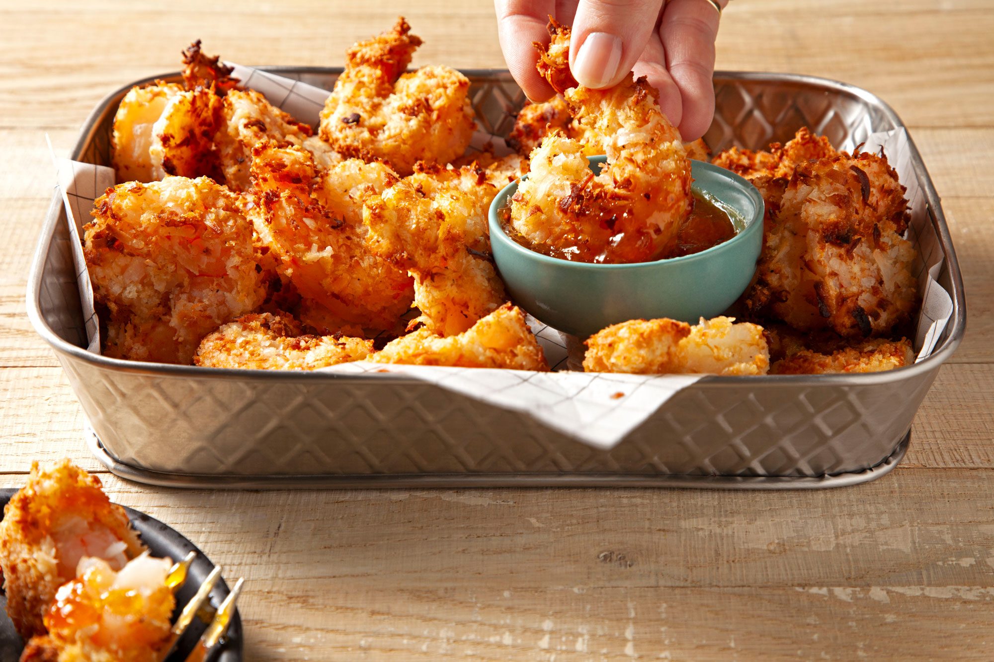 Person enjoying Air-Fryer Coconut Shrimp by dipping into a bowl of sauce