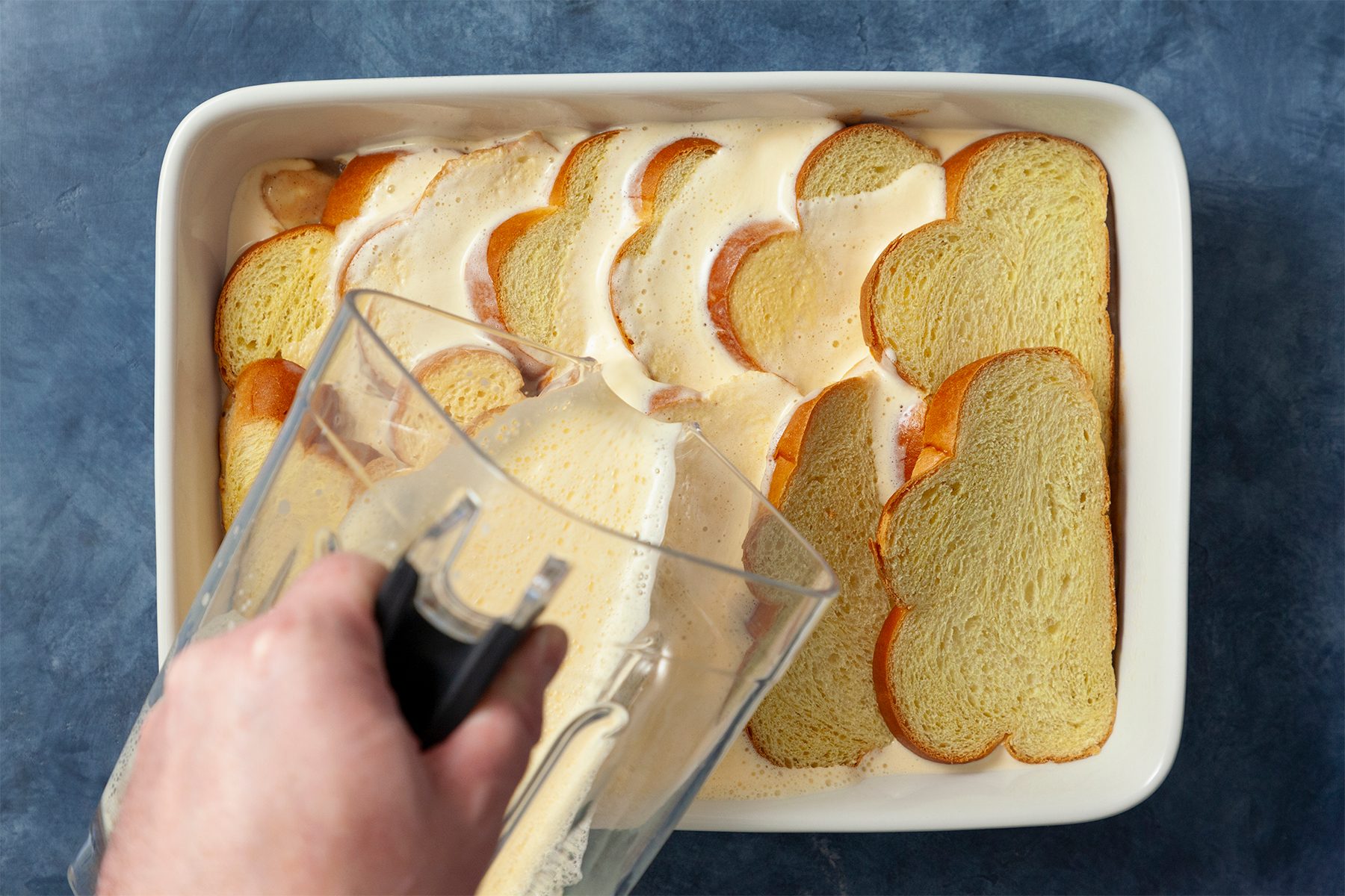 A person is pouring egg mixture in the food bowl with bread