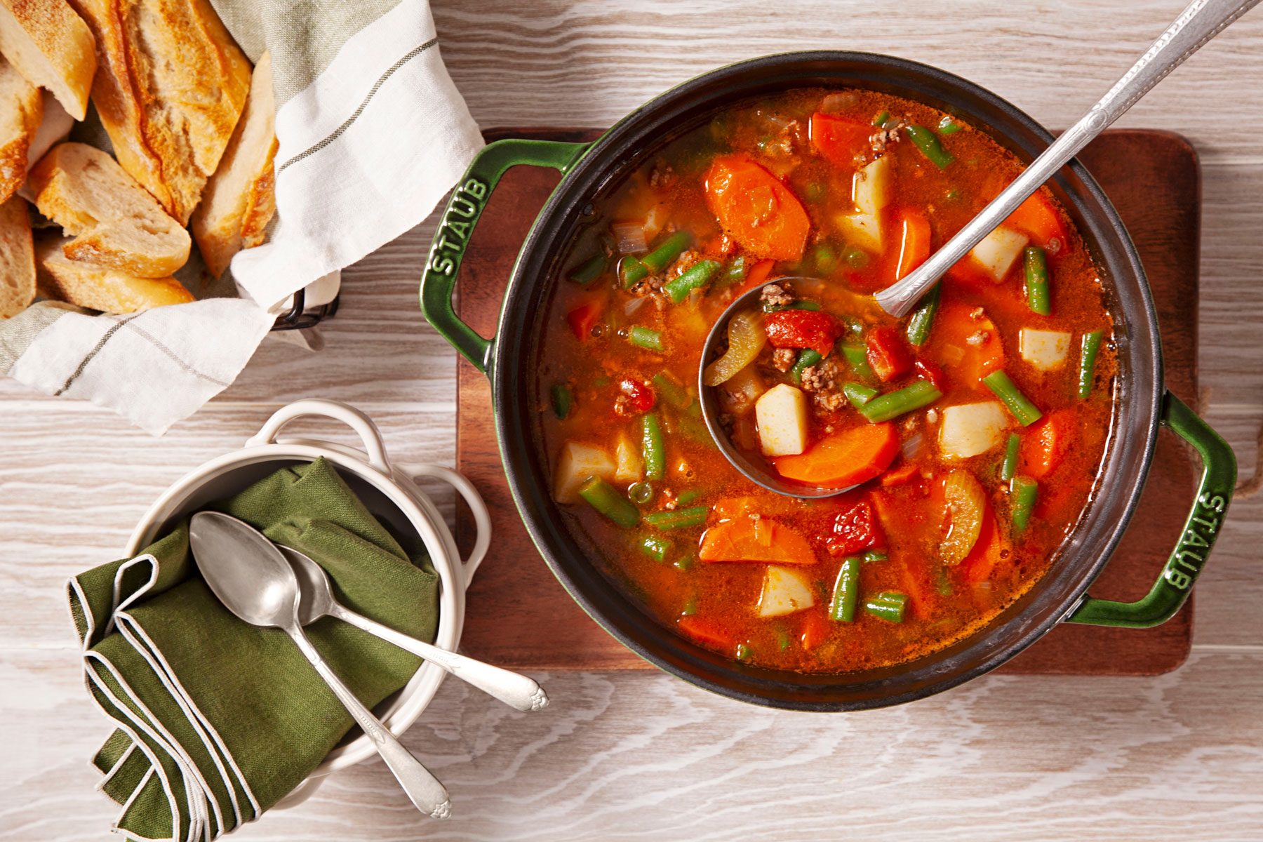 Hamburger Soup is served with bread on side, placed on a wooden table