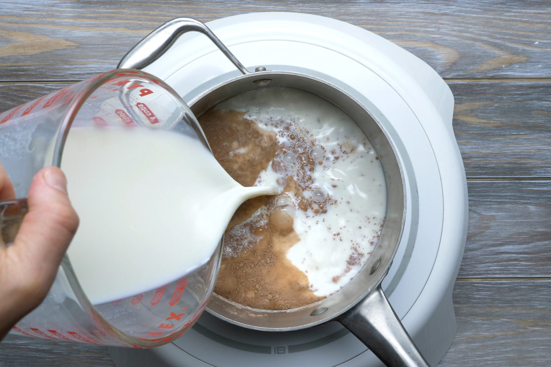 A person pouring milk in to a pan of chocolate powder