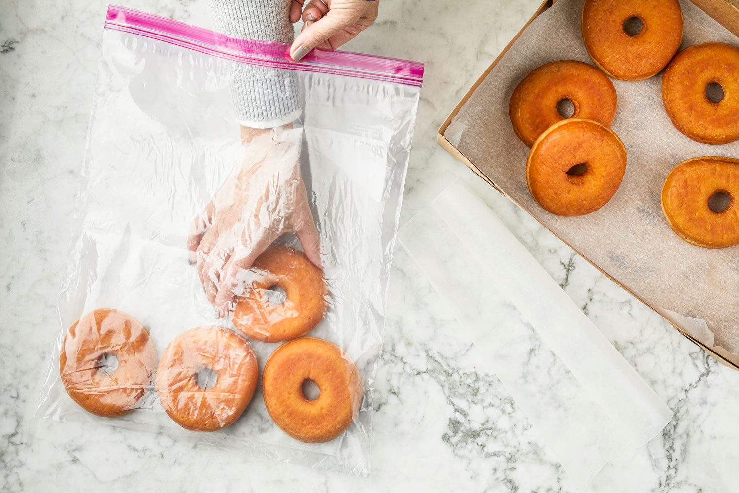 hands adding doughnuts to a plastic bag for freezing