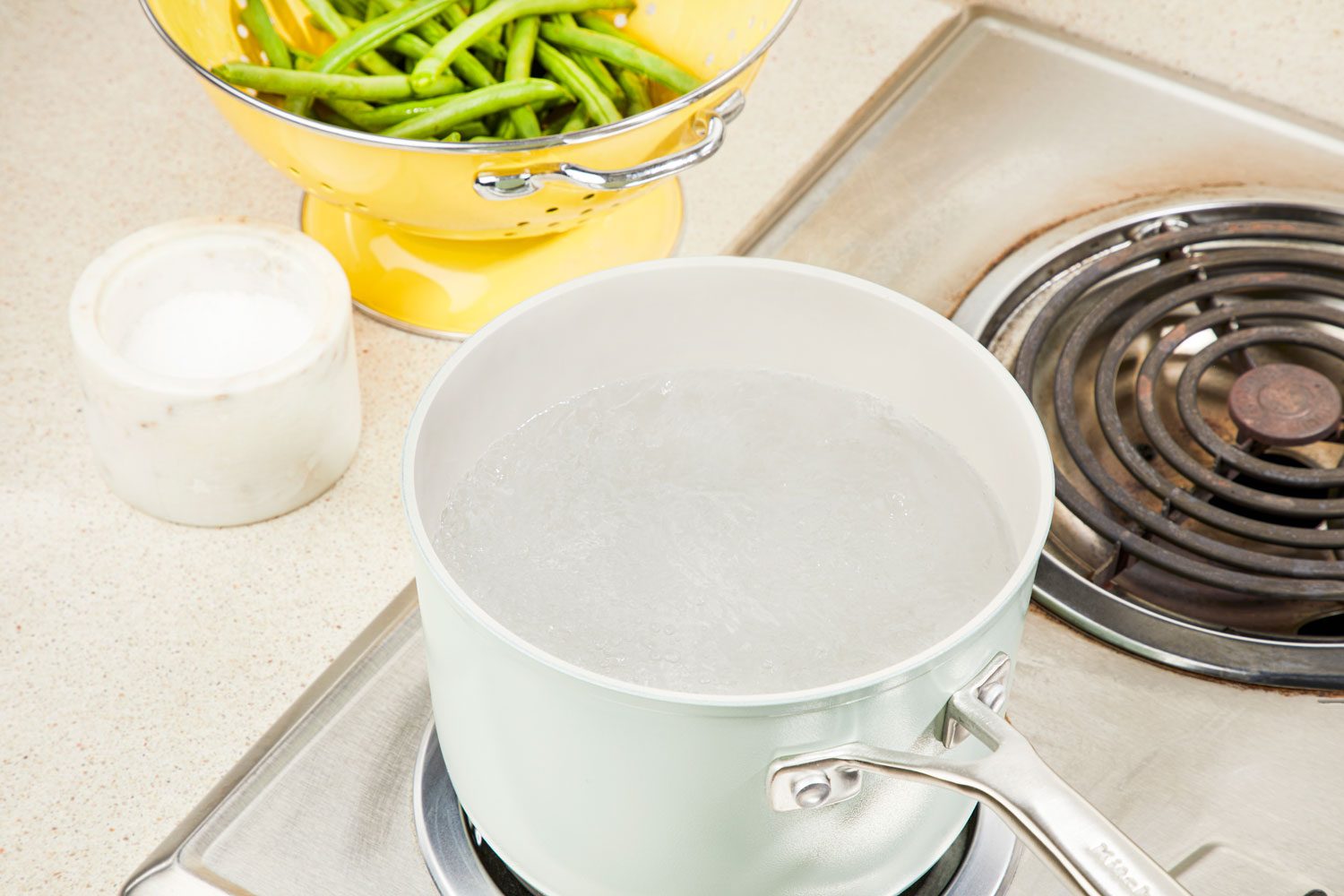 High angle view shot of a Pot of salted water being brought to a boil on the stove with rinsed green beans nearby