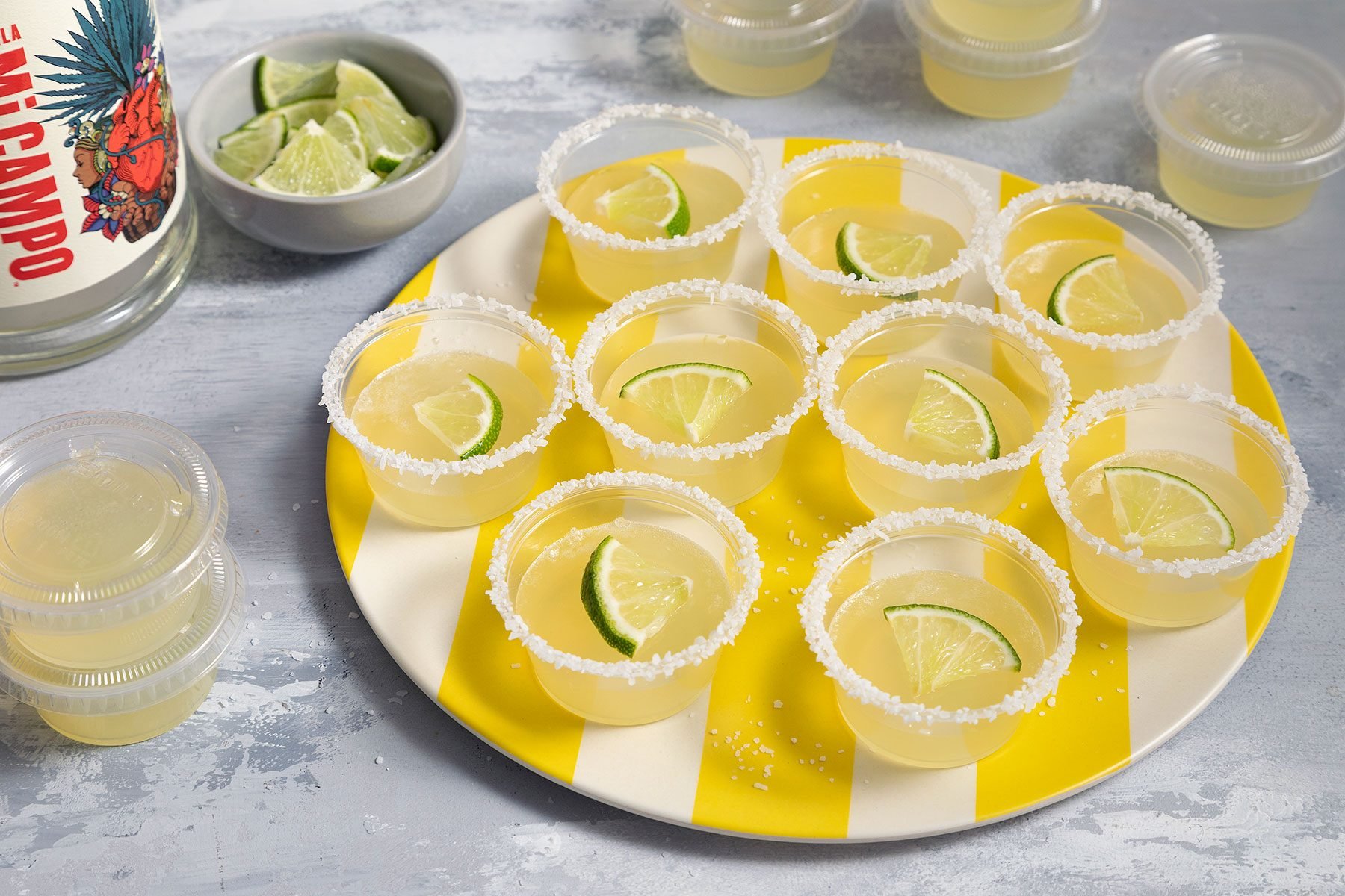 Margarita Jell O Shots served in small cups with lemon wedges on them and salt garnished on the rim of the cup