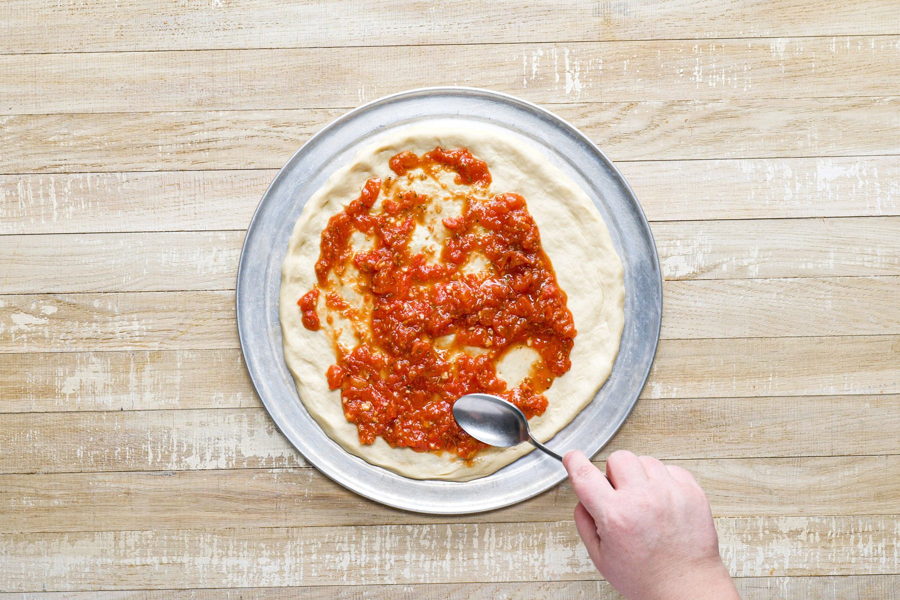 A hand holding a spoon over a pizza