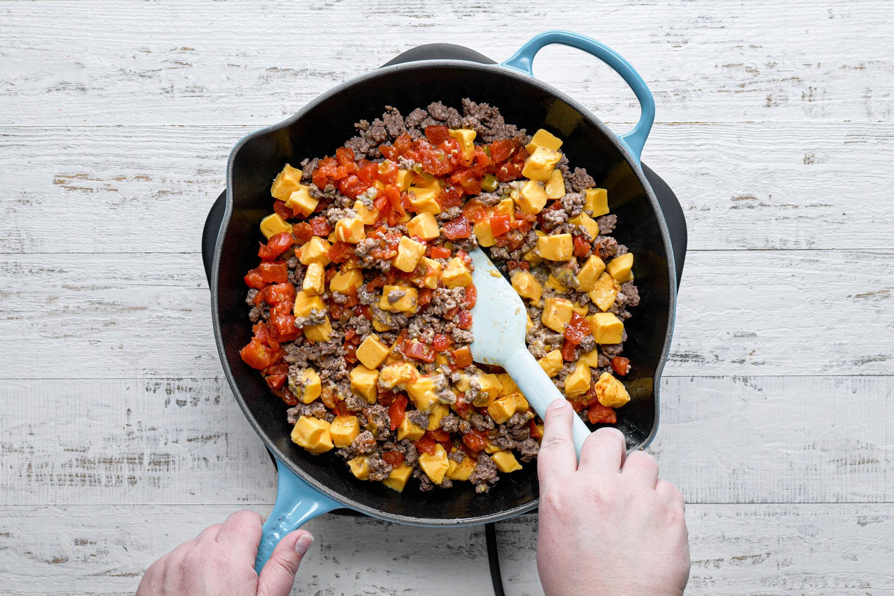 Cheese, tomatoes and chili powder mixed using a spatula in a large skillet