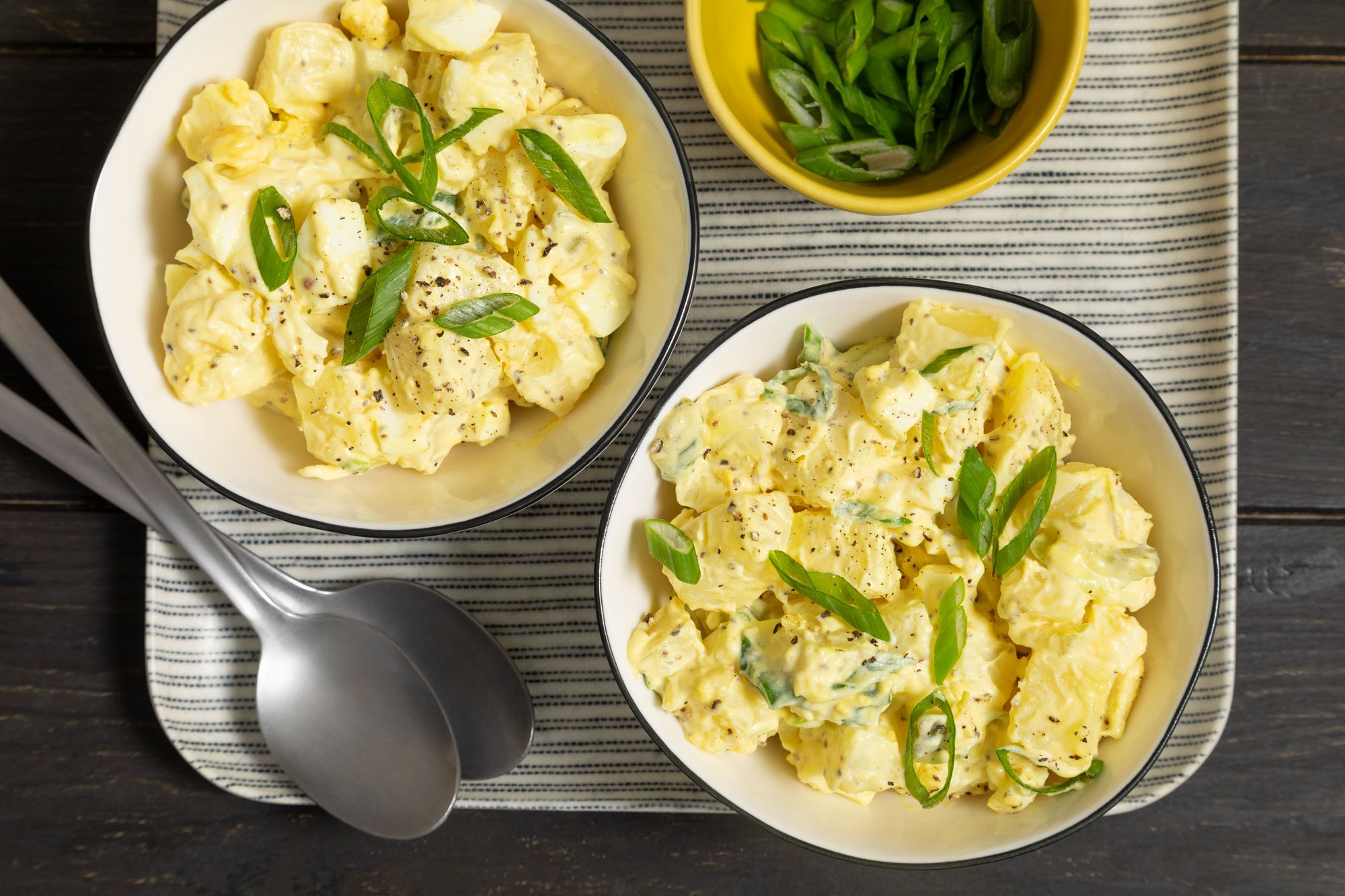 Two bowls of Southern Potato Salad topped with green onion served in a tray