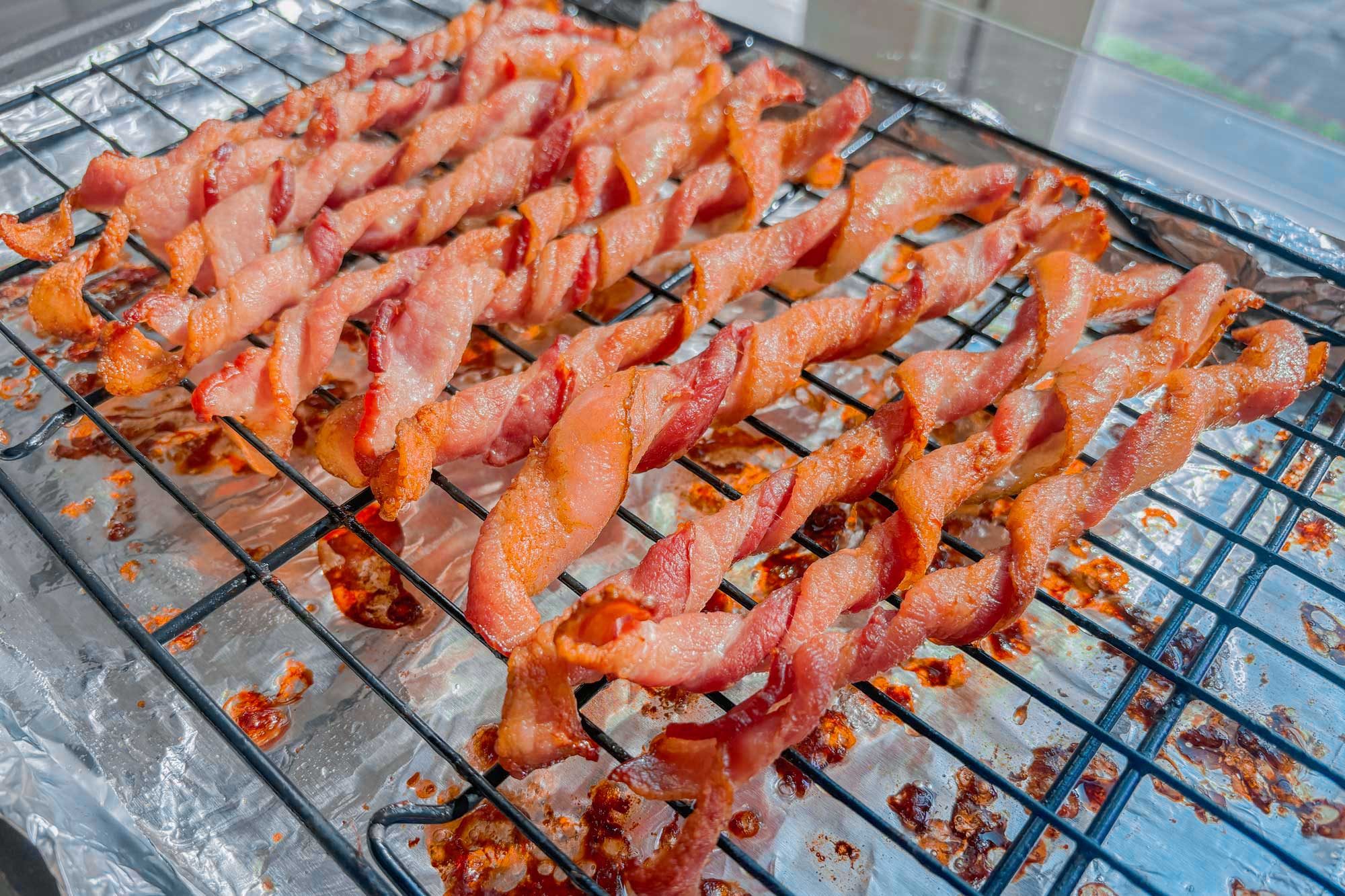 Twisted bacon enveloped in foil, positioned on a baking rack for cooking