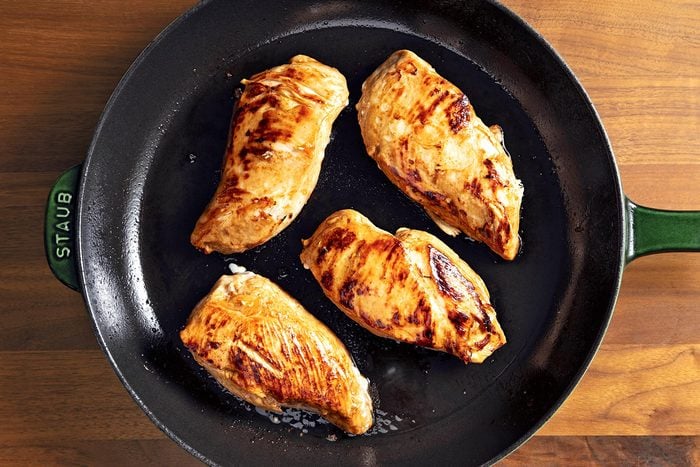 Overhead shot of cooked chicken breats; in a large overproof skillet; brown wooden background;