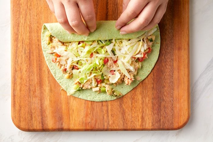 A person rolling the tuna salad tortillas