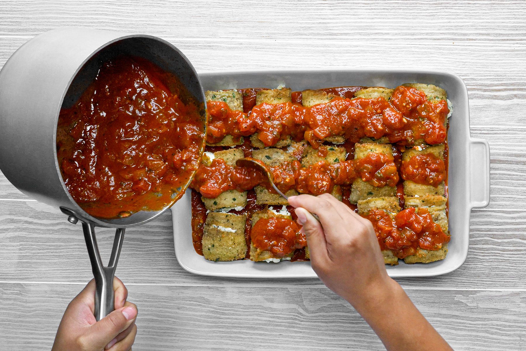 Pouring sauce from saucepan to baked eggplants 