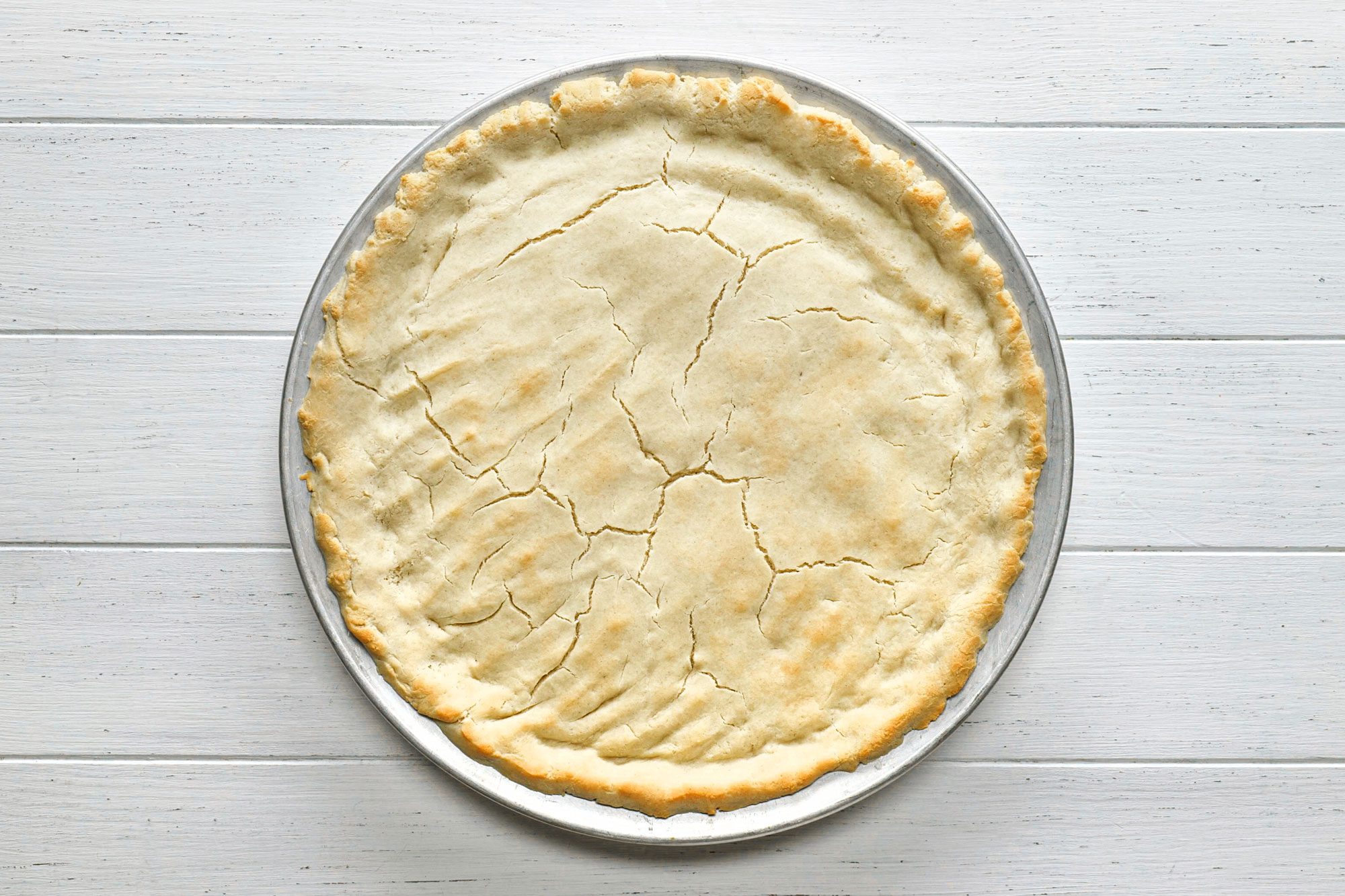 Gluten Free Pizza Crust on a pizza pan on white painted wooden surface