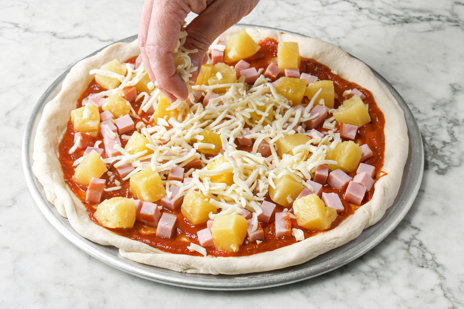 Pizza sauce, ham, pineapple and cheese on pizza dough