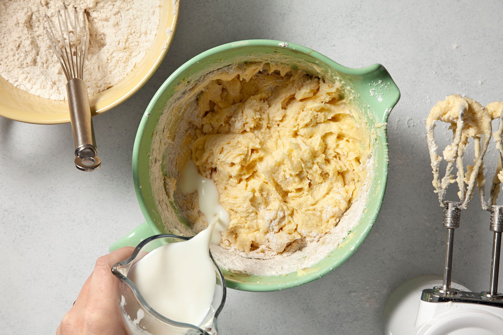 overhead shot of pouring milk into the batter in a green mixing bowl