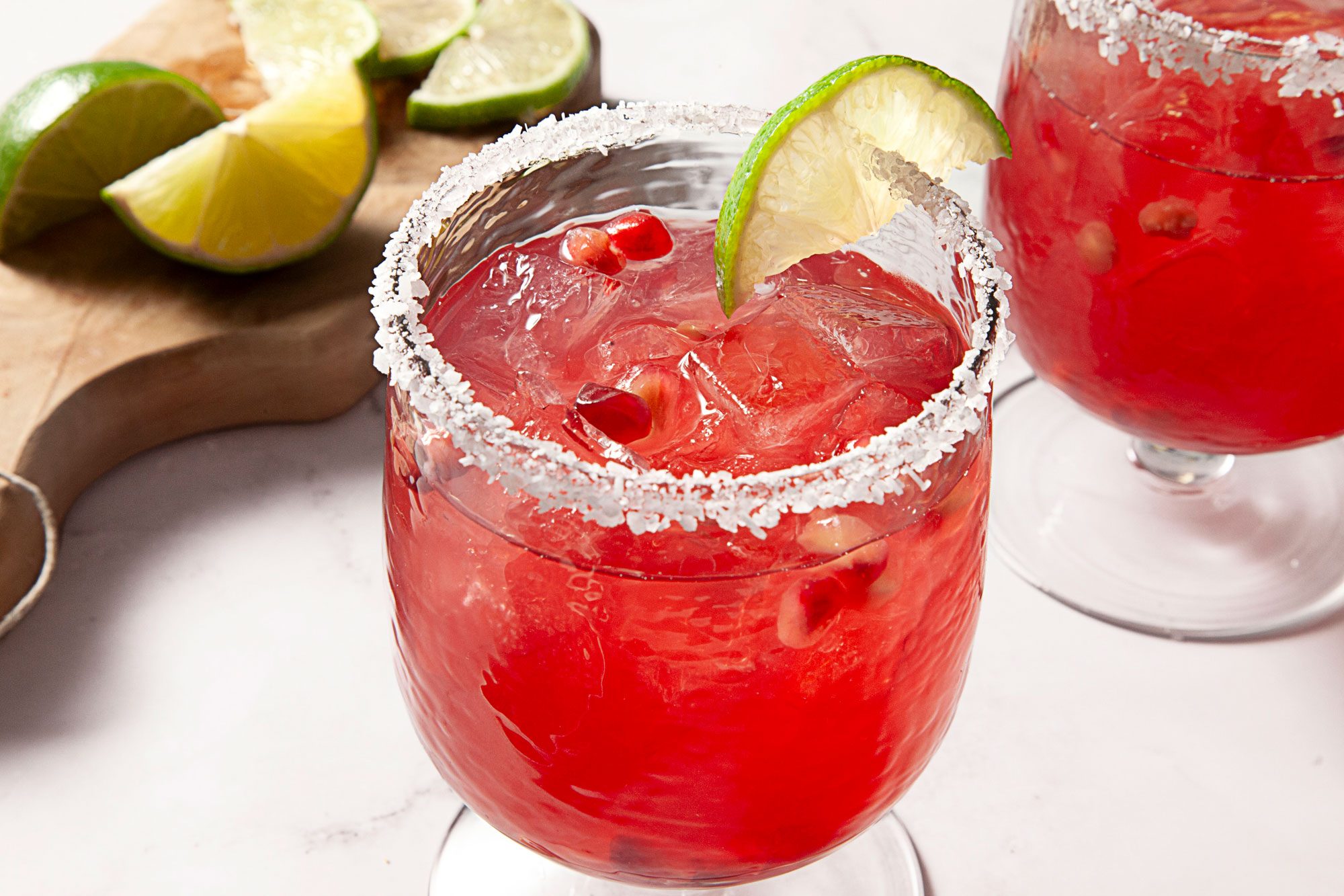 Pomegranate Margarita served in two glasses and garnished with lime wedge and pomegranate seeds