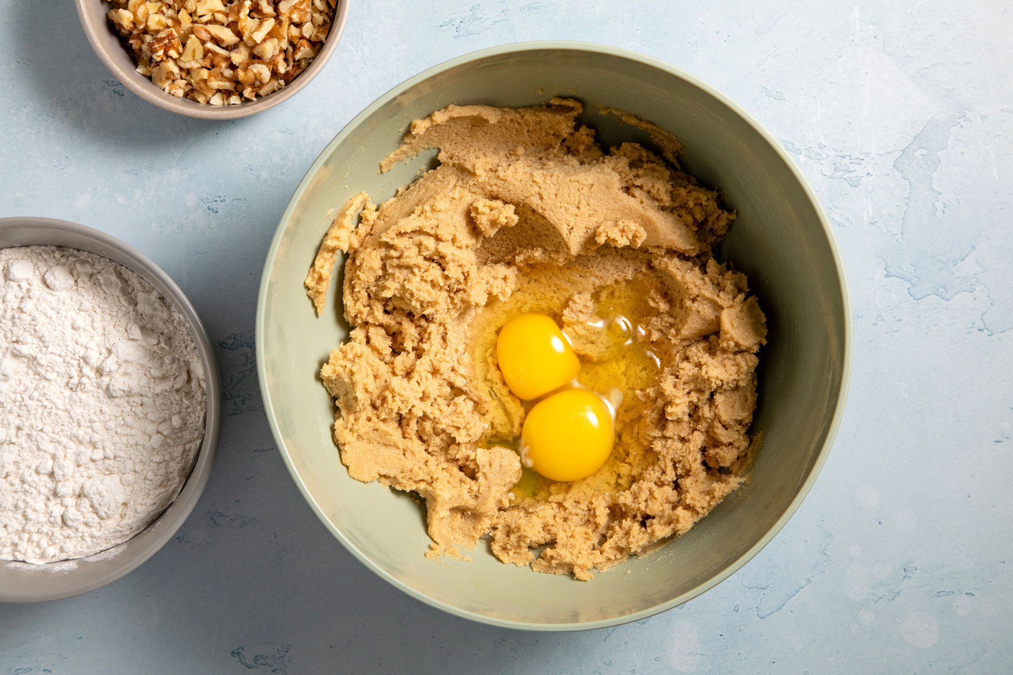 overhead shot; light blue textured background; two egg yolks in beaten mixture in a large bowl;