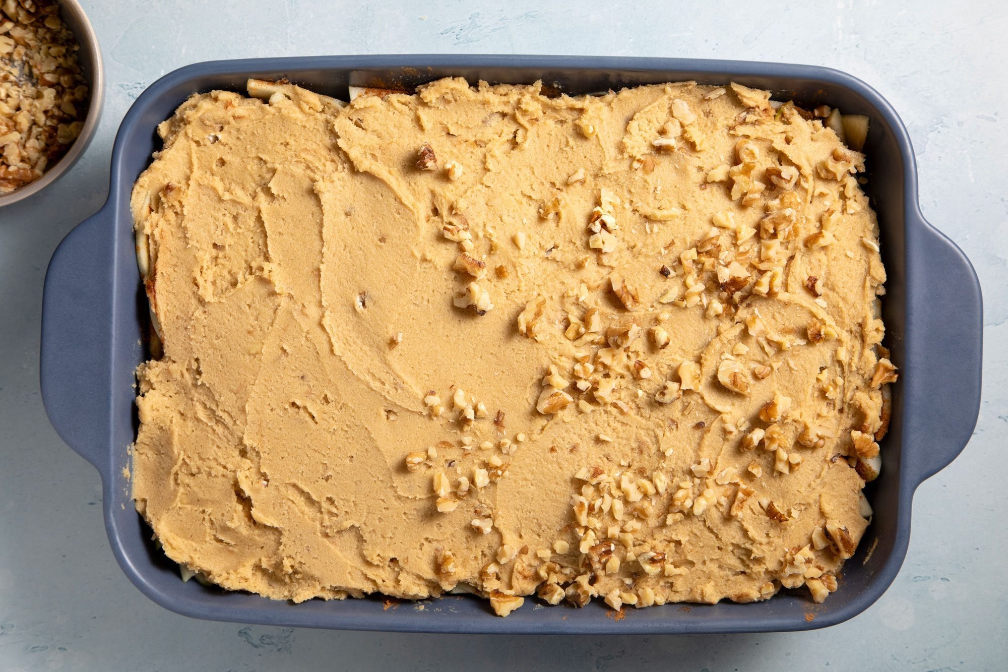 overhead shot; light blue textured background; fully spreaded beaten mixture over apples in baking dish;