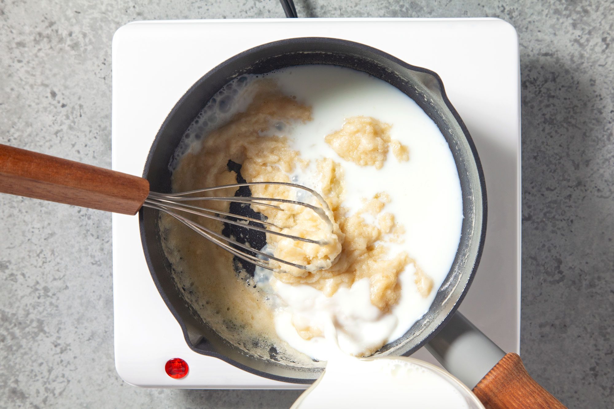Overhead shot of gradually whisk in milk; induction; marble background;