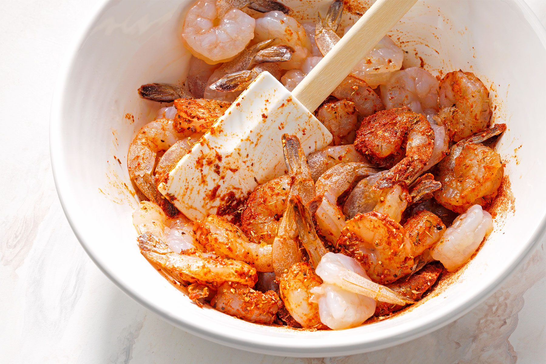 Overhead shot of added shrimp in mixture; toss to coat; spatula; white marble background;
