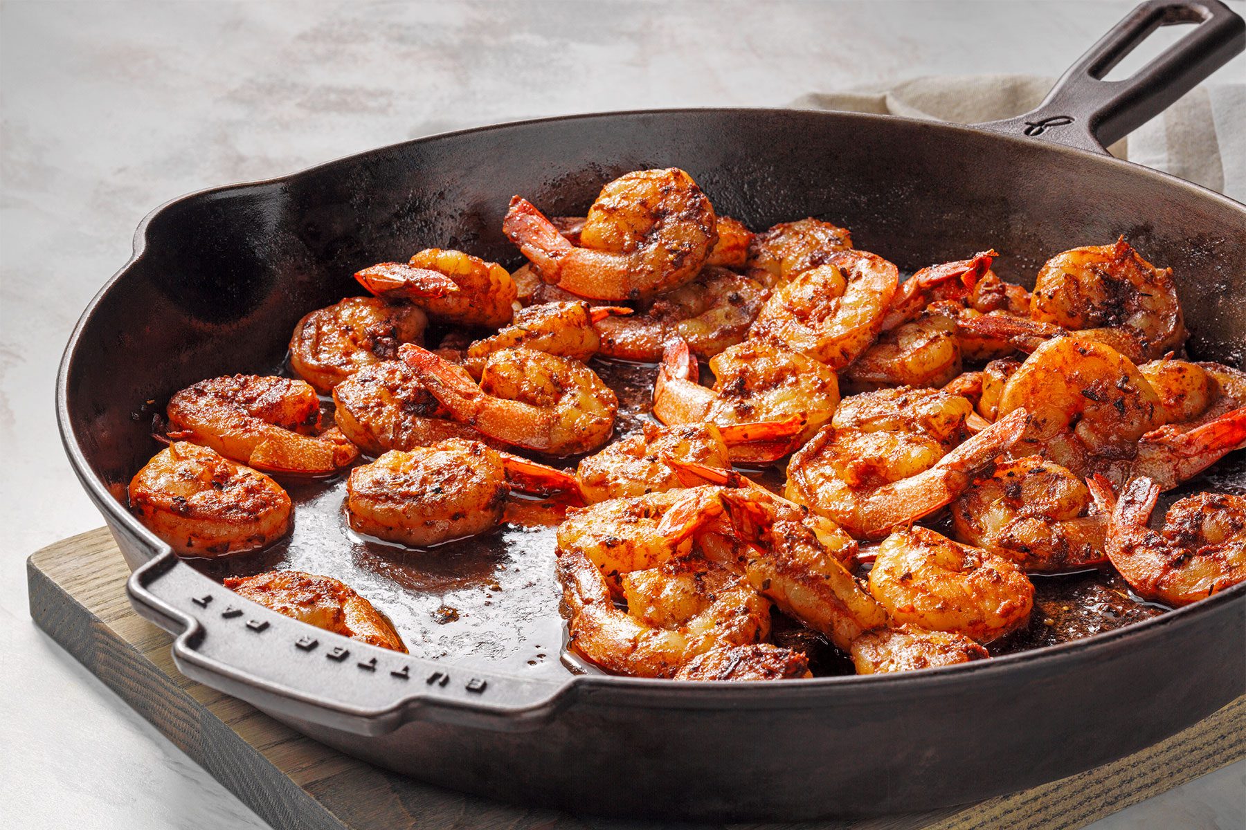 Table view shot of Blackened Shirmp; wooden base; kitchen towel; white marble background;