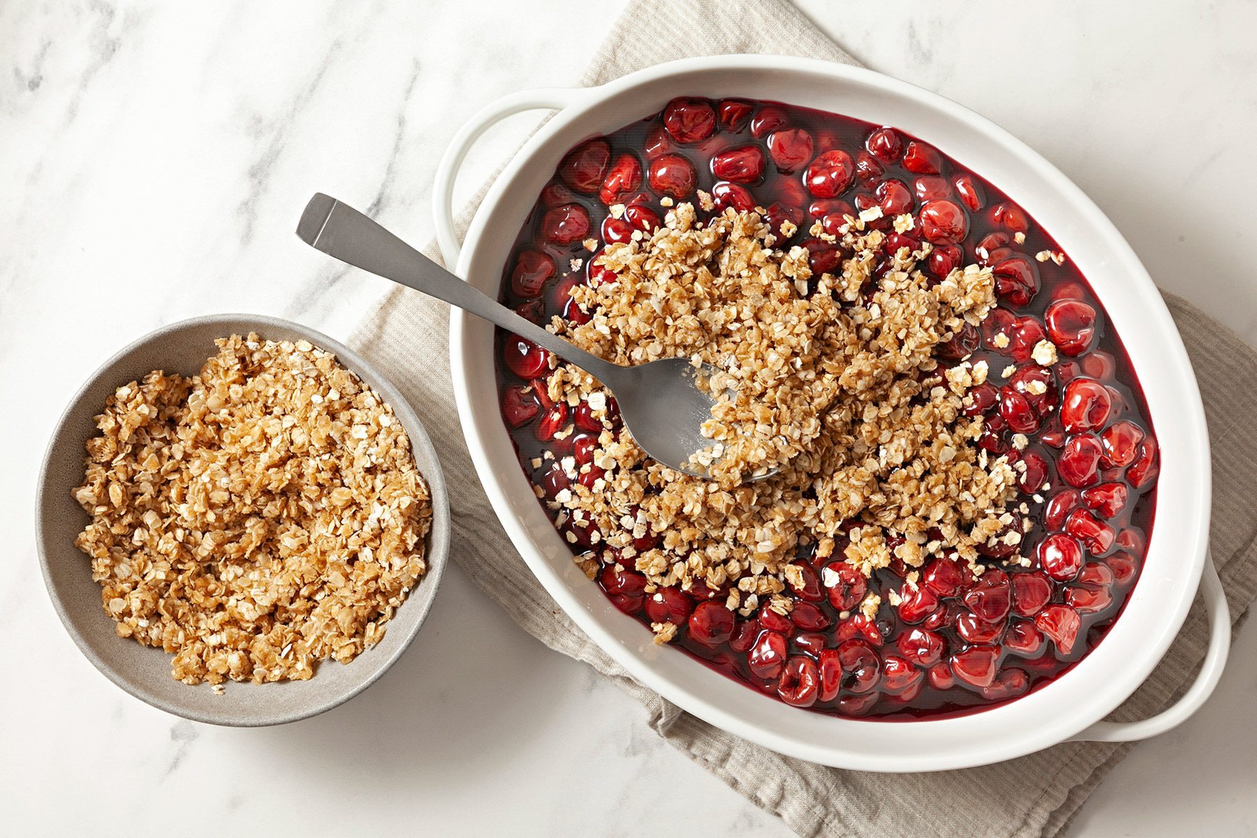 overhead shot; white background; sprinkled topping over filling in large serving dish; topping in small bowl