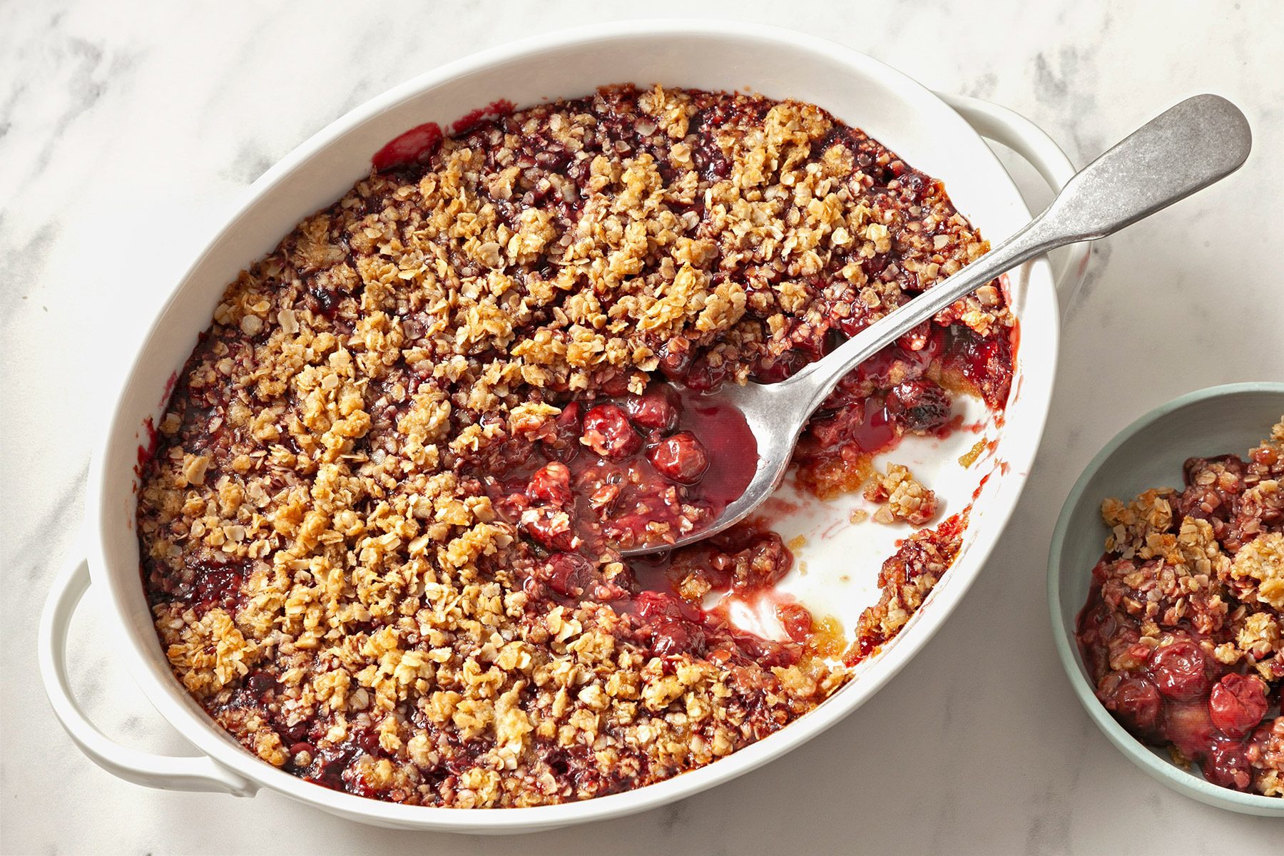 3/4th shot; white background; Cherry Crisp in oval serving dish with large silver spoon