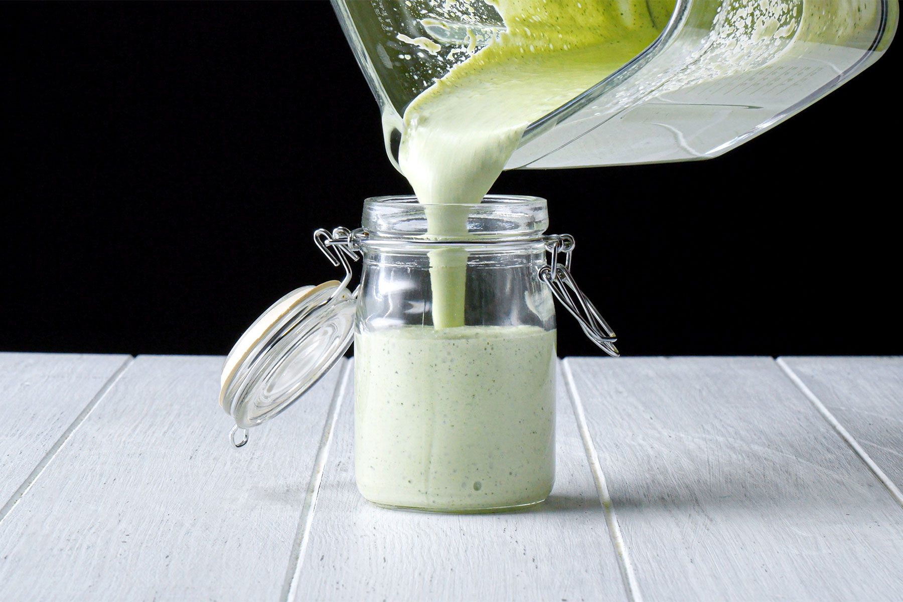 Table view shot of transfering the smooth mixture into a glass jar; white wooden background;