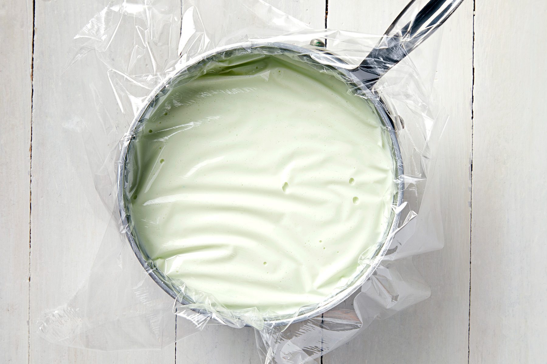 overhead shot; white background; Press plastic wrap onto surface of custard over saucepan;
