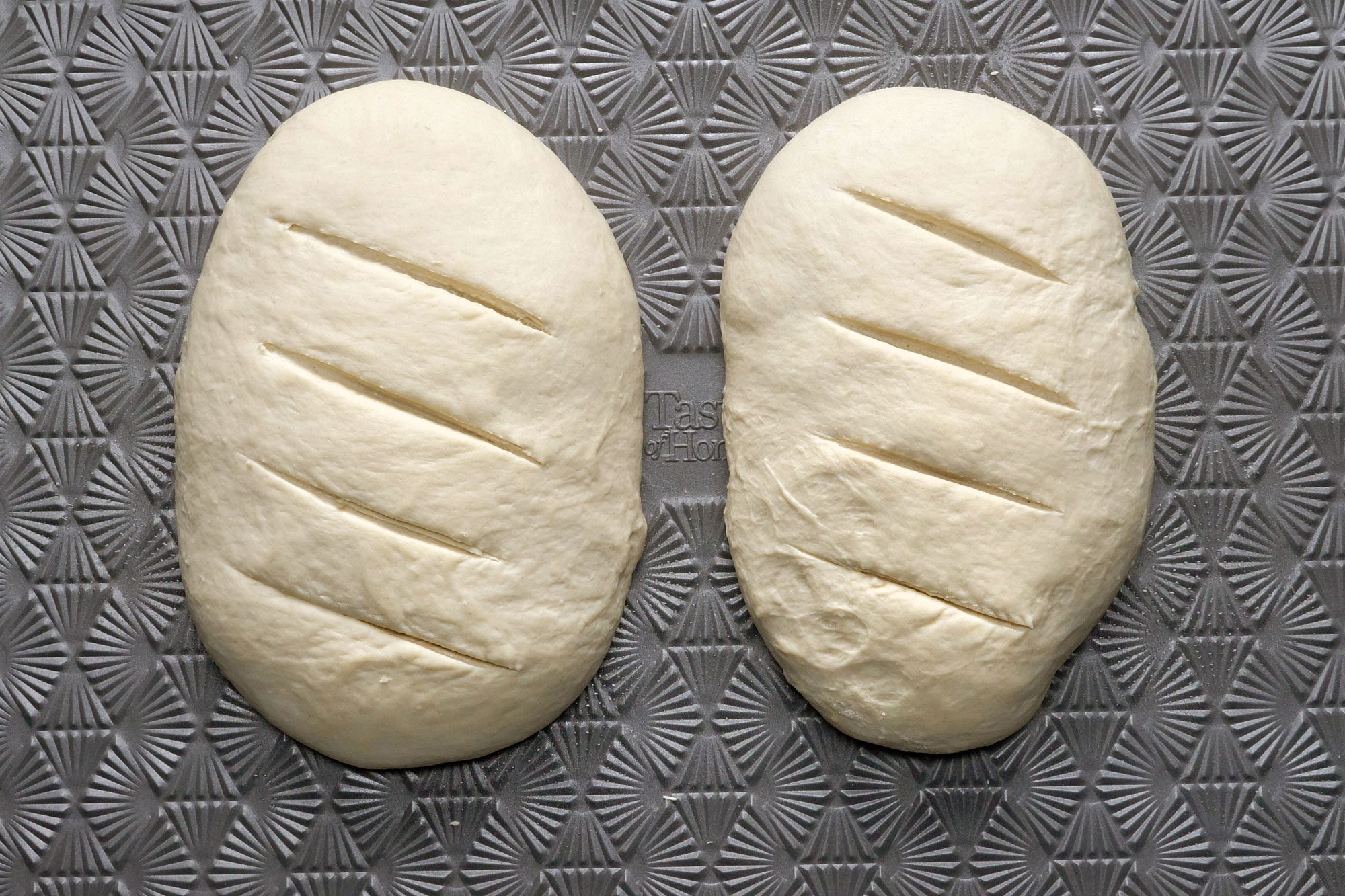 Two loafs slashed by knife on a baking sheet
