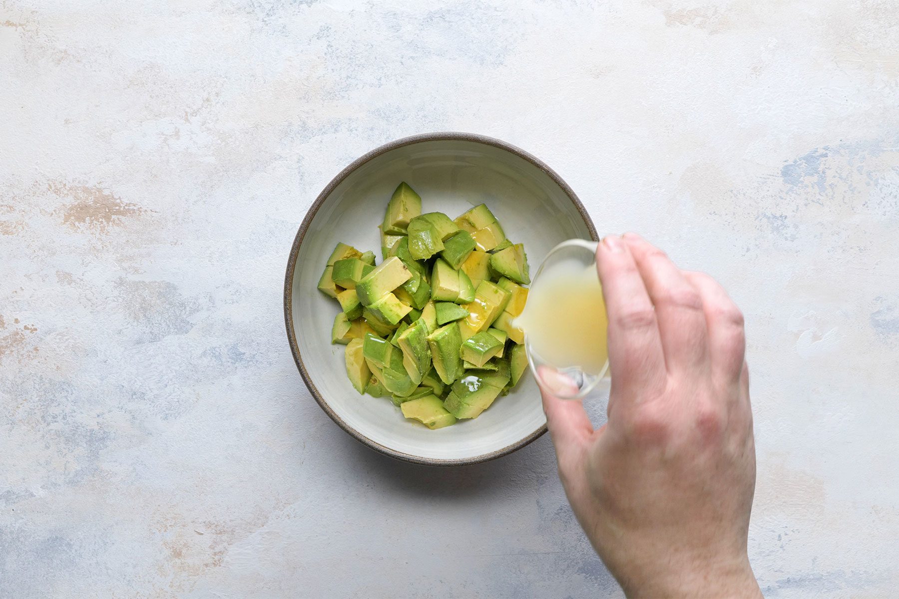 Overhead shot a small bowl; gently toss avocados with lime juice; white marble background;