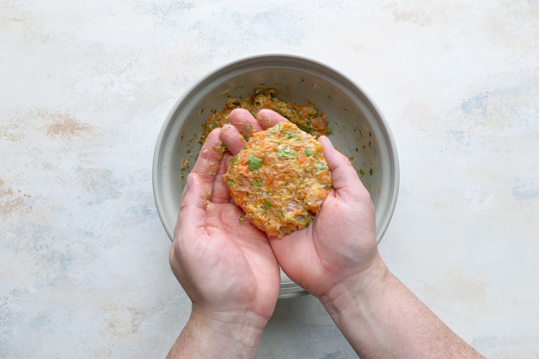 Overhead shot of shape the mixture into four thick patties; white marble background;