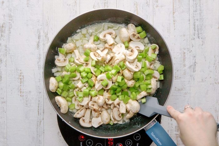 overhead shot of sauteing the onions, celery and mushrooms in a large skillet; wooden background;