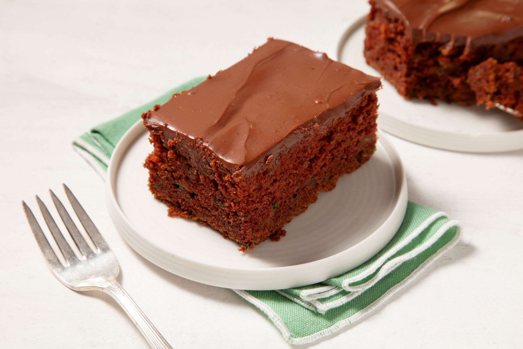 3/4th angle shot of Zucchini Brownie; served on a small plate; napkin; forks; marble background;